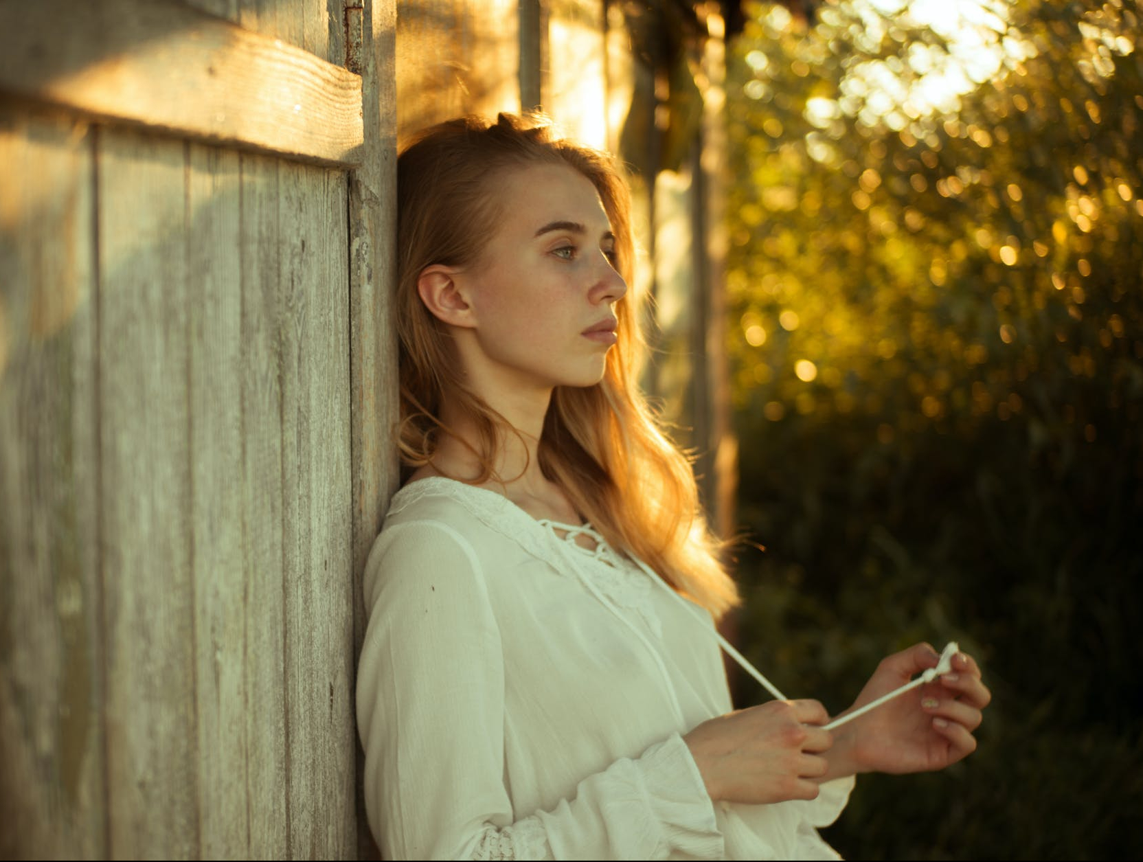 woman wearing white top leaning on wooden wall