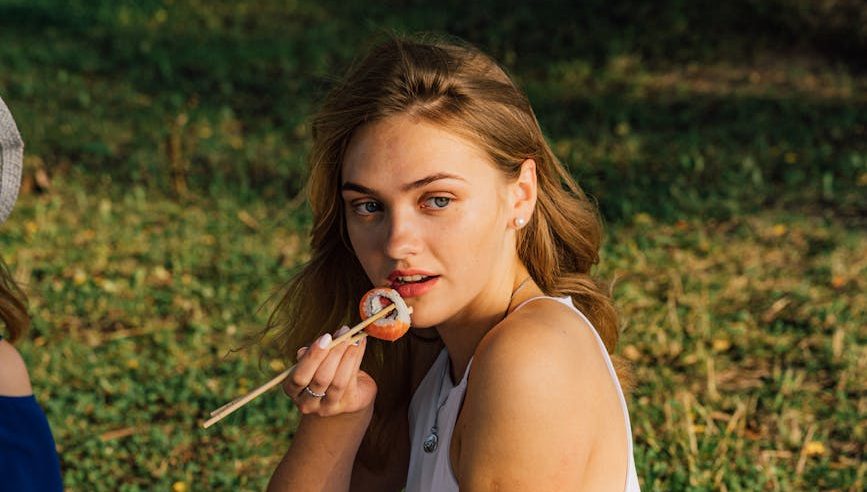 woman in white tank top and blue pants eating sushi